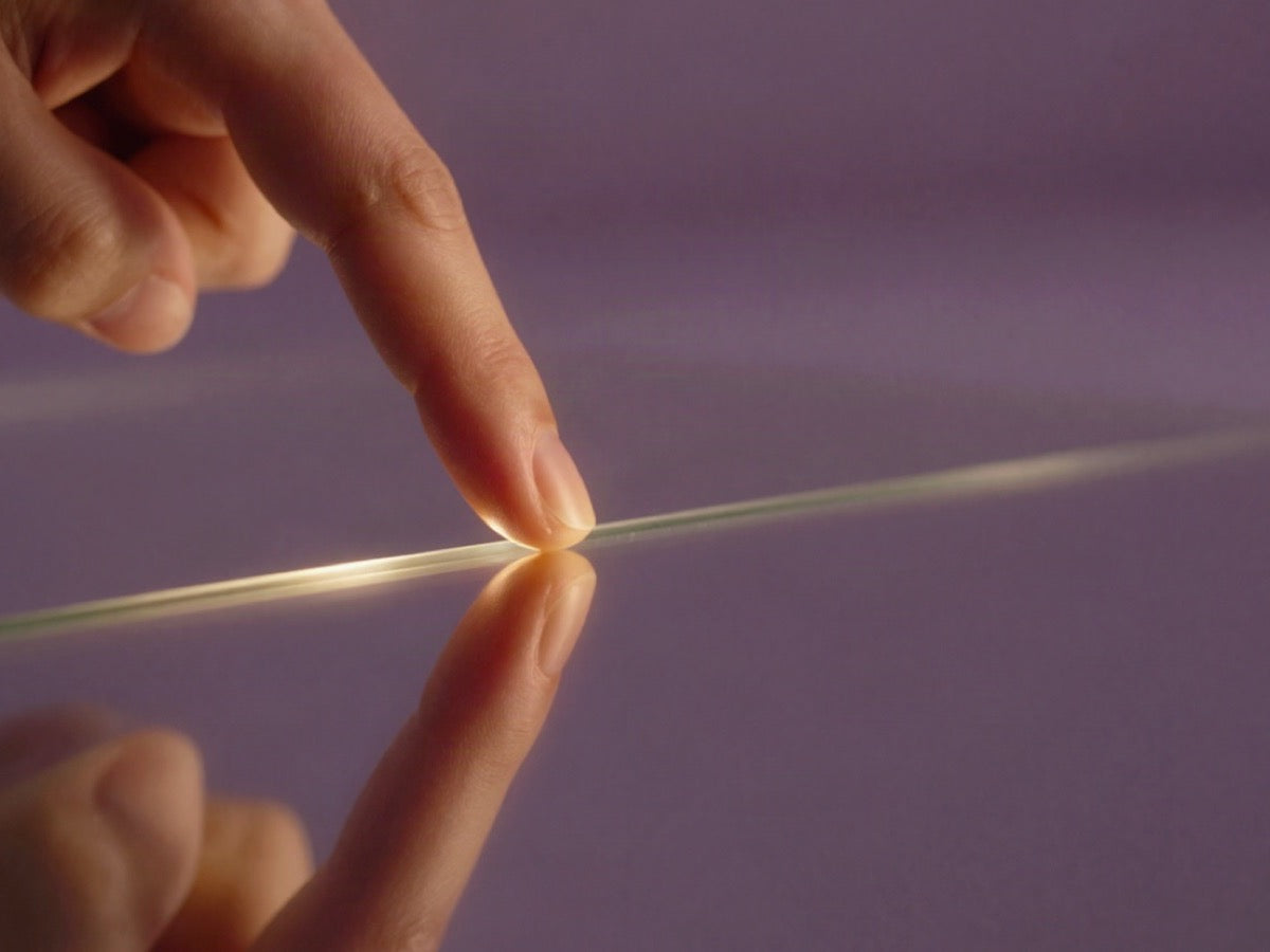 Fingertip touching a line of light on a lilac surface