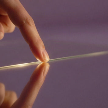 Fingertip touching a line of light on a lilac surface
