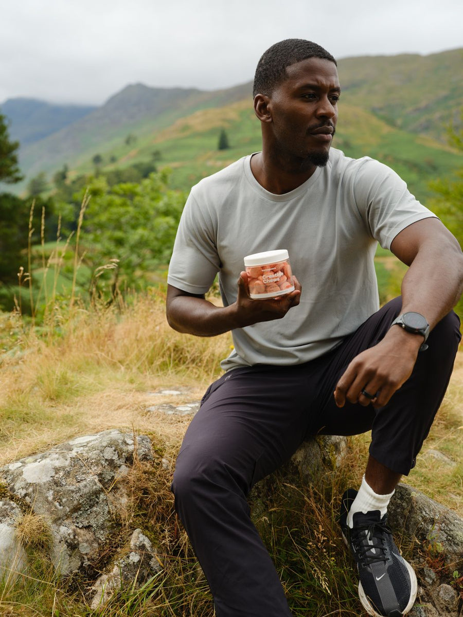 A man sitting on a rock with a tub of Creatine Chews, looking across the valley